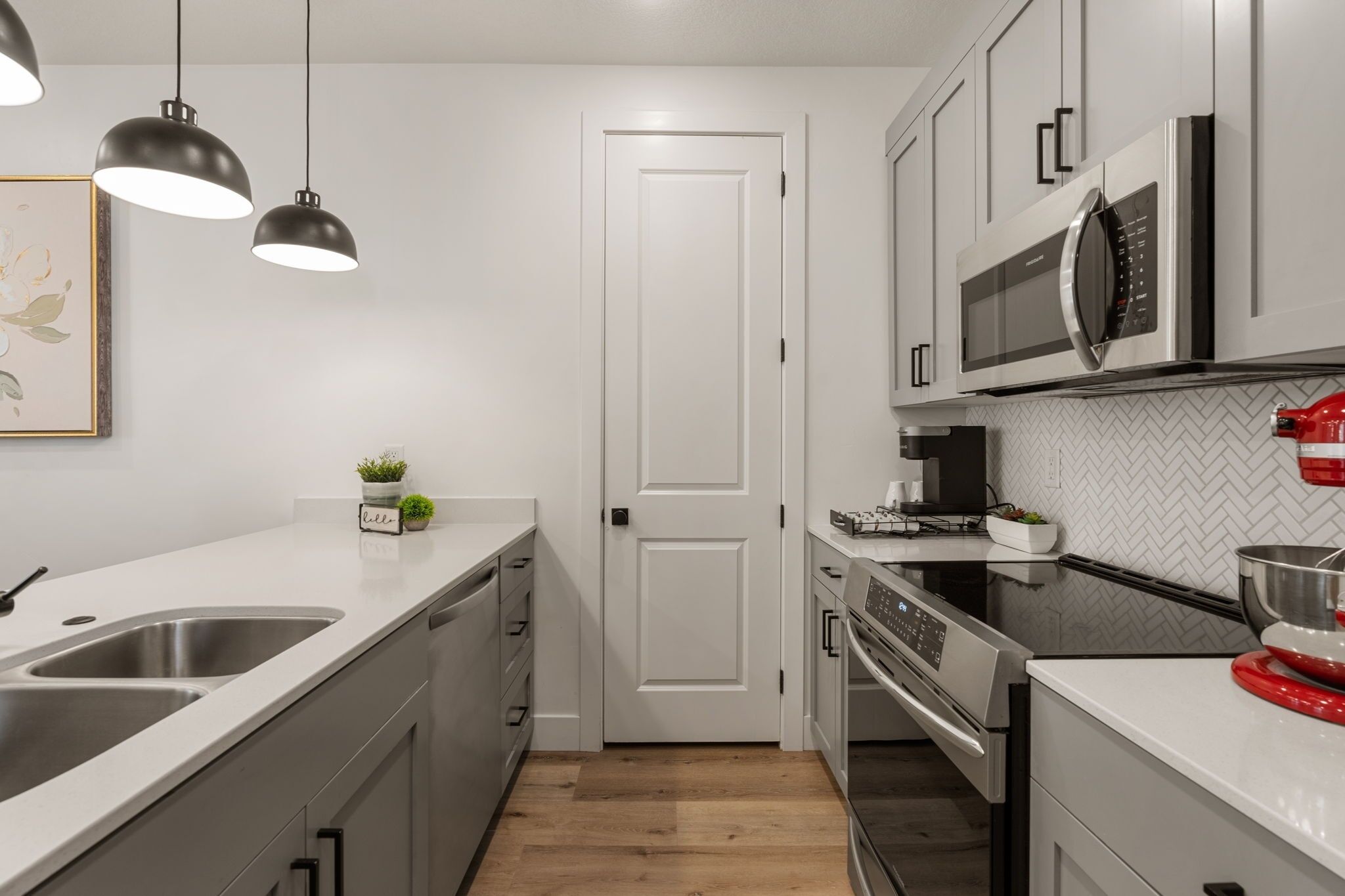 Een moderne keuken met roestvrijstalen apparatuur, een dubbele spoelbak, hangende lampen en een backsplash met een hongaars geblokte motief.