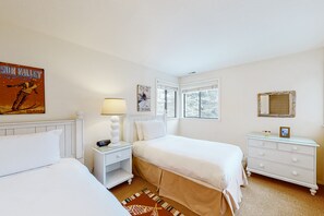 Relax in this stylish room with two single beds, a nightstand, and a dresser, surrounded by framed artwork and a large window.
