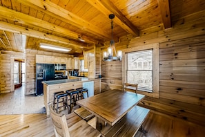 Cozy cabin with a large dining table, kitchen area, and bar, surrounded by large windows and wooden accents.