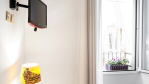 A wall-mounted TV, a lamp with a classical design, and a window with a view of a balcony with flowers. - RESIDENZA SANSONI charming and easy (Roma)