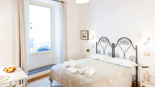 A bedroom with a wooden ceiling, a bed with white linens, a bedside table with a lamp, and a window with curtains. - RESIDENZA SANSONI charming and easy (Roma)