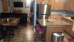 A compact kitchen with wooden cabinets, a stainless steel refrigerator, a granite countertop, and a bar stool.