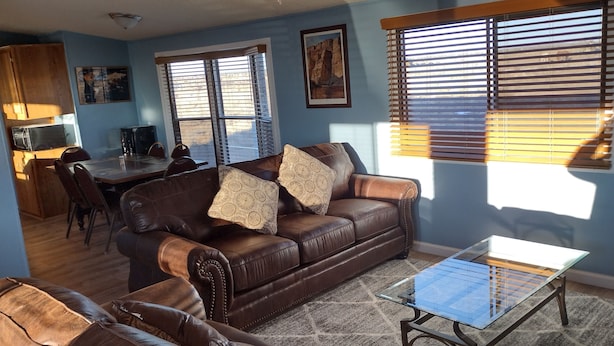 A living room with a brown leather sofa, a glass coffee table, and a dining area with a table and chairs.