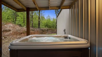 Een hottub in een open omgeving, met een houten terras en metalen wanden, omgeven door bomen en een rotsachtig landschap.