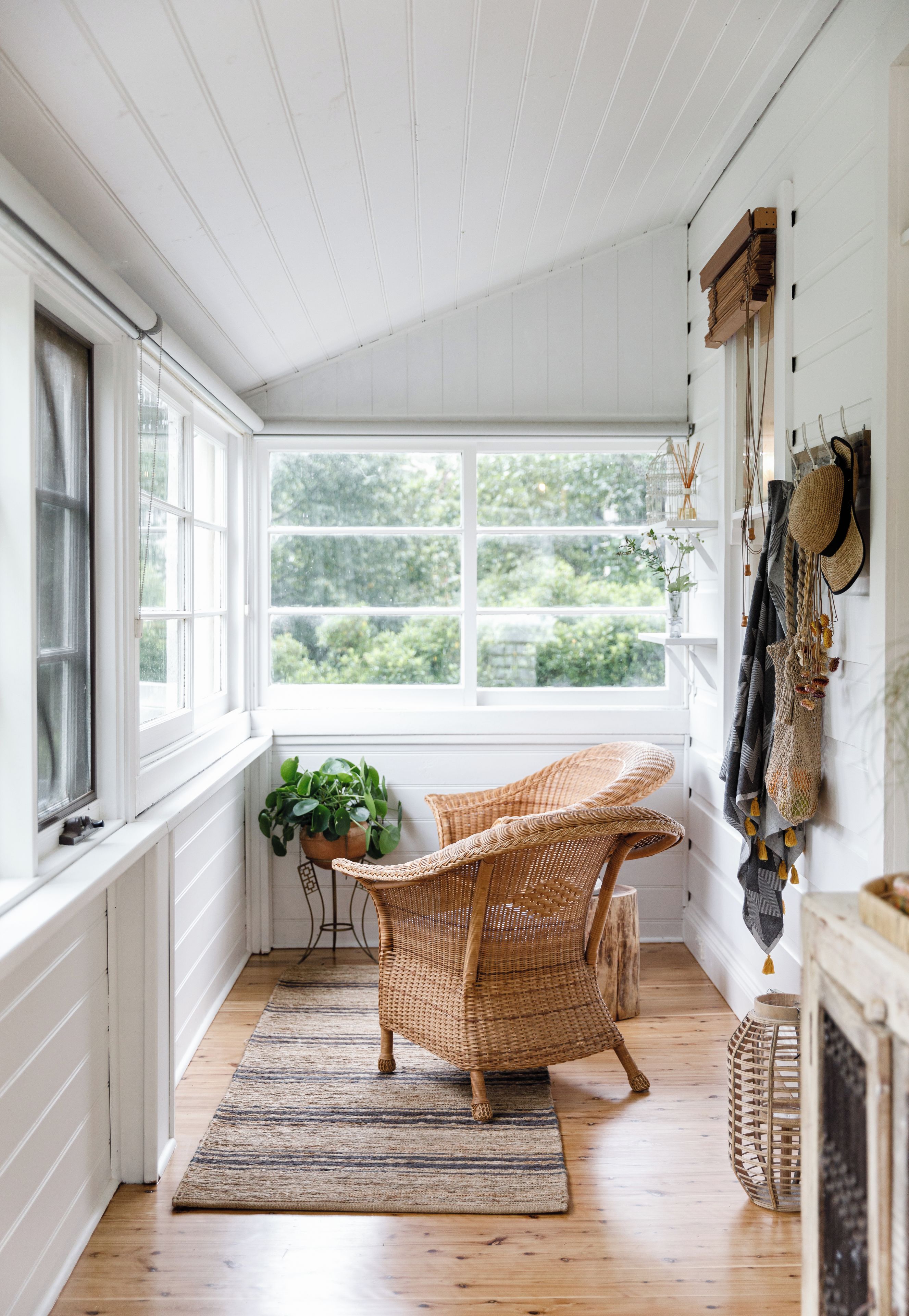 A cozy room with a large window, wicker chairs, a small table, and a hanging hat rack.