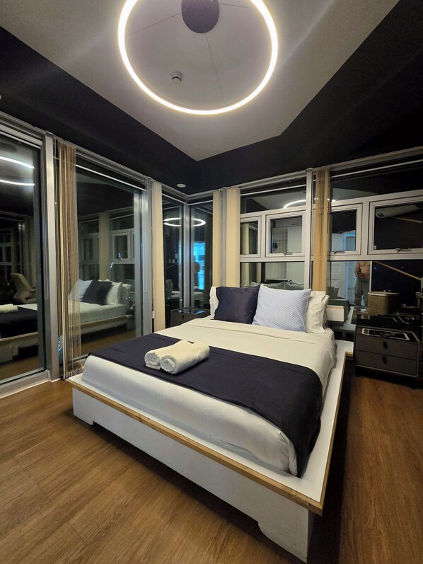 A modern hotel room with a large bed, a bedside table, a mirror, and a circular light fixture on the ceiling.