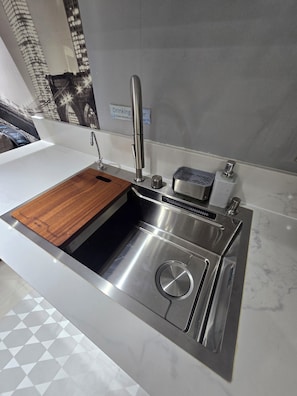 Une cuisine moderne dotée d’un évier en acier inoxydable, d’une planche à découper en bois et d’un four encastré.