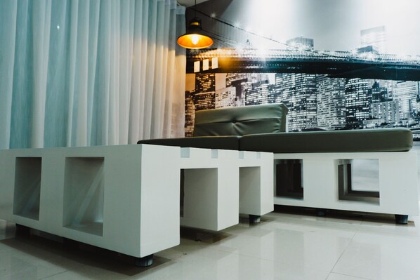 Un'area di accoglienza dal design moderno, con una reception bianca, una poltrona in pelle e un murale raffigurante un panorama cittadino.