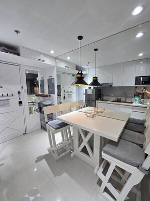Une cuisine moderne avec des meubles blancs, un îlot central doté de sièges, des luminaires suspendus et un micro-ondes visible.