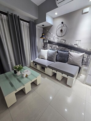Un salon moderne avec un canapé, une table basse en verre et une lampe fixée au mur.