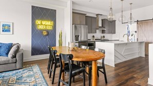 A modern kitchen with grey cabinets, a stainless steel refrigerator, and a white island. There is a dining area with a wooden table and black chairs. - Rosedale ~ Huge New Condo ~ 3BR + Bonus ~ 3 Miles to Broadway ~ Near GEODIS Park (Nashville)