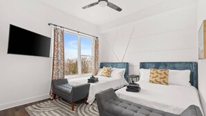 A modern hotel room with a bed, a desk, a chair, a flat-screen TV, and a ceiling fan. - Rosedale ~ Huge New Condo ~ 3BR + Bonus ~ 3 Miles to Broadway ~ Near GEODIS Park (Nashville)