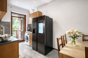 A modern kitchen with a built-in washer and dryer, a black refrigerator, and a dining area with a vase of flowers. - Family Room Yellow & Blue   Two Bedrooms (ROMA)