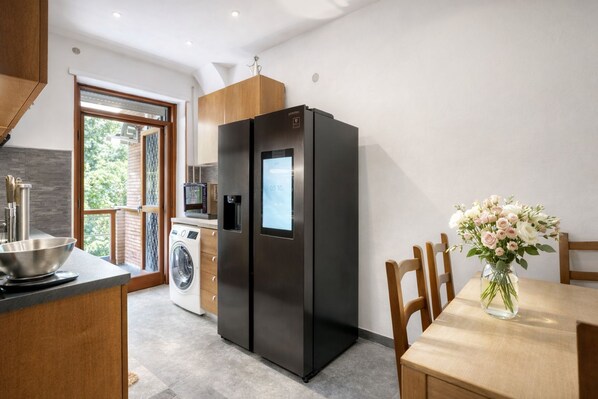 A modern kitchen with a built-in washer and dryer, a black refrigerator, and a dining area with a vase of flowers.
