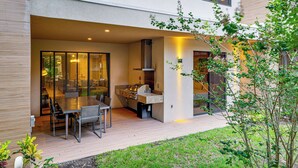 An outdoor kitchen area with a grill, dining table, and chairs, surrounded by a wooden deck and greenery. - Magic Villas Townhome ~ 5 Mi to Disney Parks! (Kissimmee)