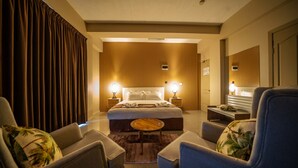 Una habitación de hotel con una cama grande, dos mesitas de noche con lámparas, una mesa de centro redonda y dos sillones.