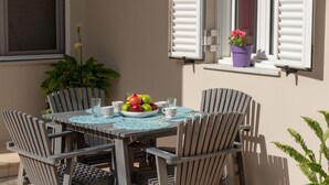 An outdoor dining area with a table and chairs, a potted plant, and a window with shutters. - Aria 1 - Vacation apartment in Crete, 100 m from the seaside (Kolimbári)