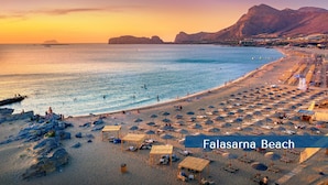 A beach with umbrellas and sun loungers, a clear sky, and mountains in the background. - Aria 1 - Vacation apartment in Crete, 100 m from the seaside (Kolimbári)