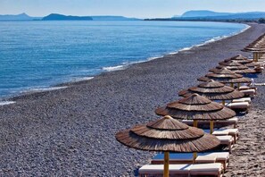 A beach with rows of sun loungers and thatched umbrellas along the shoreline.