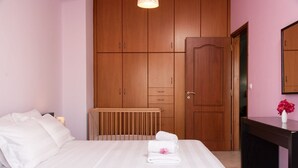 A bedroom with a bed, a wooden wardrobe, a radiator, and a desk with a vase of flowers. - Aria 1 - Vacation apartment in Crete, 100 m from the seaside (Kolimbári)