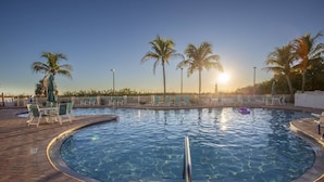 Ein Swimmingpool mit Liegestühlen und Palmen, umgeben von einer Ziegelterrasse.