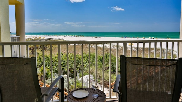 Ein Balkon mit Blick auf einen Strand, ein Tisch mit Teller und Glas sowie zwei Stühle.