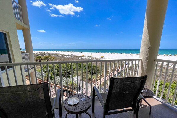 Un balcon avec vue sur la plage, comprenant un espace salon extérieur et une bouteille de vin.