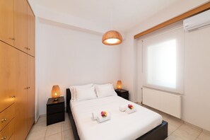 Quarto com cama, duas mesas de cabeceira, luminária pendente, radiador e janela com persianas.
