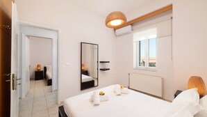 A hotel room with a bed, a bedside table, a mirror, a window, and a hanging light fixture. - Aria 2 - Vacation apartment in Crete, 100 m from the seaside (Kolimbári)