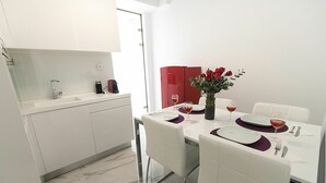 A modern kitchen with white cabinets, a marble countertop, and a dining area with white chairs and a table set for two. - Aria 3 - Vacation Apartment in Crete, 100 m from the seaside (Kolimbári)