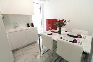 A modern kitchen with white cabinets, a marble countertop, and a dining area with white chairs and a table set for two.