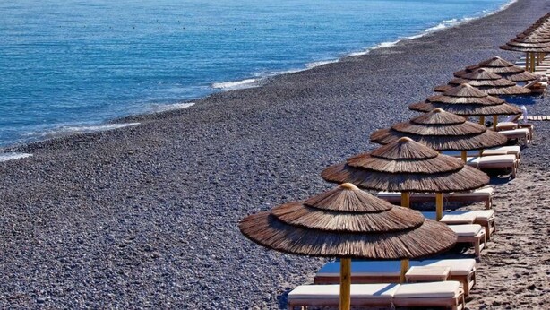 A beach with rows of sun loungers and thatched umbrellas along the shoreline. - Aria 3 - Vacation Apartment in Crete, 100 m from the seaside (Kolimbári)