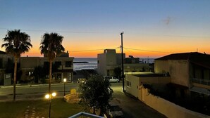 A coastal residential area at dusk with buildings, a street, and a view of the sea. - Aria 3 - Vacation Apartment in Crete, 100 m from the seaside (Kolimbári)
