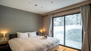 Ein modernes Hotelzimmer mit einem großen Bett, Holzboden und Blick auf eine verschneite Landschaft durch eine Schiebeglastür.