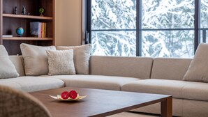 Ett modernt vardagsrum med en beige soffa, ett träbord som används som soffbord och som pryds av en dekorativ detalj, samt en bokhylla med diverse föremål.