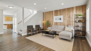 A living room with a sofa, two armchairs, a coffee table, and a wooden accent wall.
