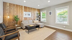 A modern living room with a wooden accent wall, a grey sofa, a black coffee table, and a large window with blinds.