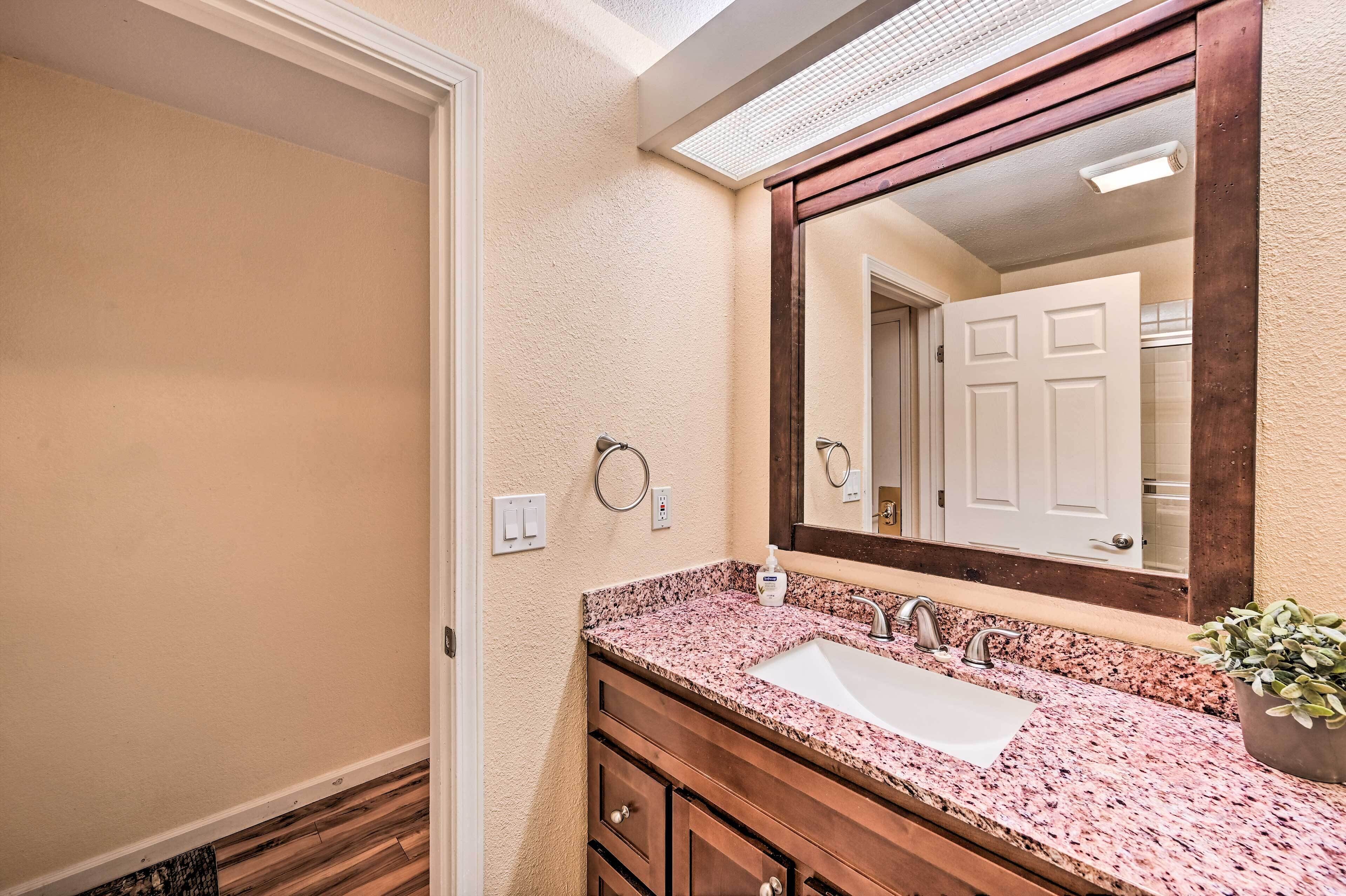 Une salle de bain avec un comptoir en granit, un lavabo, un miroir et un meuble-lavabo en bois.