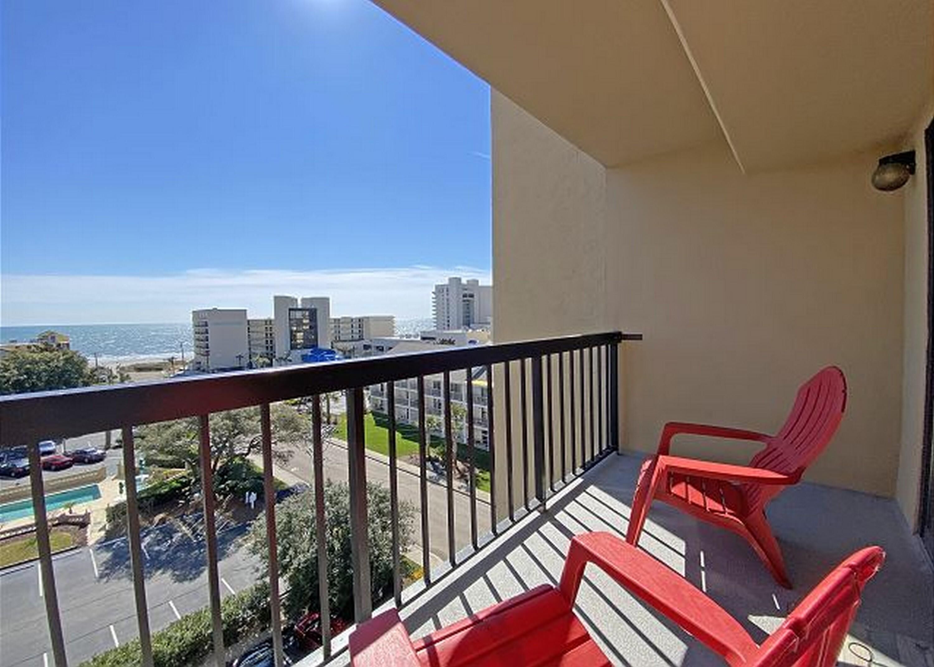 Ein Balkon mit Blick auf Strand und Stadtlandschaft, mit zwei roten Stühlen und einem Pool im Hintergrund.