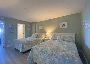 Un dormitorio con dos camas, una mesita de noche, una lámpara y una puerta que da a otra habitación.