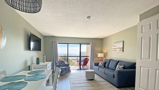 A spacious living area with a dining table, a sofa, and a balcony with a view. - Ocean Dunes by Palmetto Vacations (Myrtle Beach)