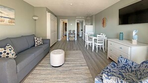 A modern living room with a grey sofa, ottoman, and patterned armchair. A dining area with a white table and chairs is visible in the background. - Ocean Dunes by Palmetto Vacations (Myrtle Beach)