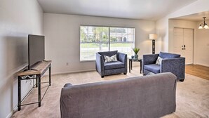 A living room with a large window, two armchairs, a sofa, a TV on a stand, and a lamp. - Breezy Cape Coral Oasis, Covered Lanai & BBQ (Cape Coral)