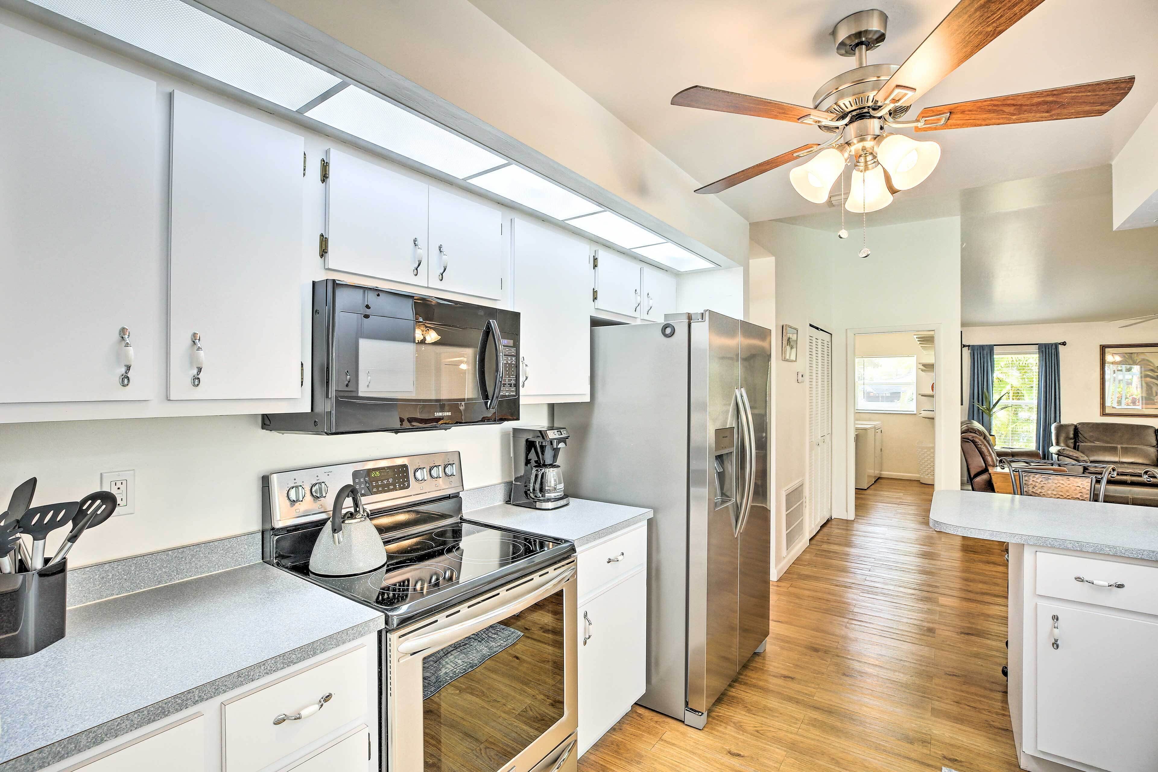 A modern kitchen with white cabinets, stainless steel appliances, a gas stove, and a ceiling fan.
