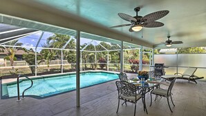 A covered outdoor pool area with a table and chairs, ceiling fans, and a view of the surrounding landscape. - Breezy Cape Coral Oasis, Covered Lanai & BBQ (Cape Coral)