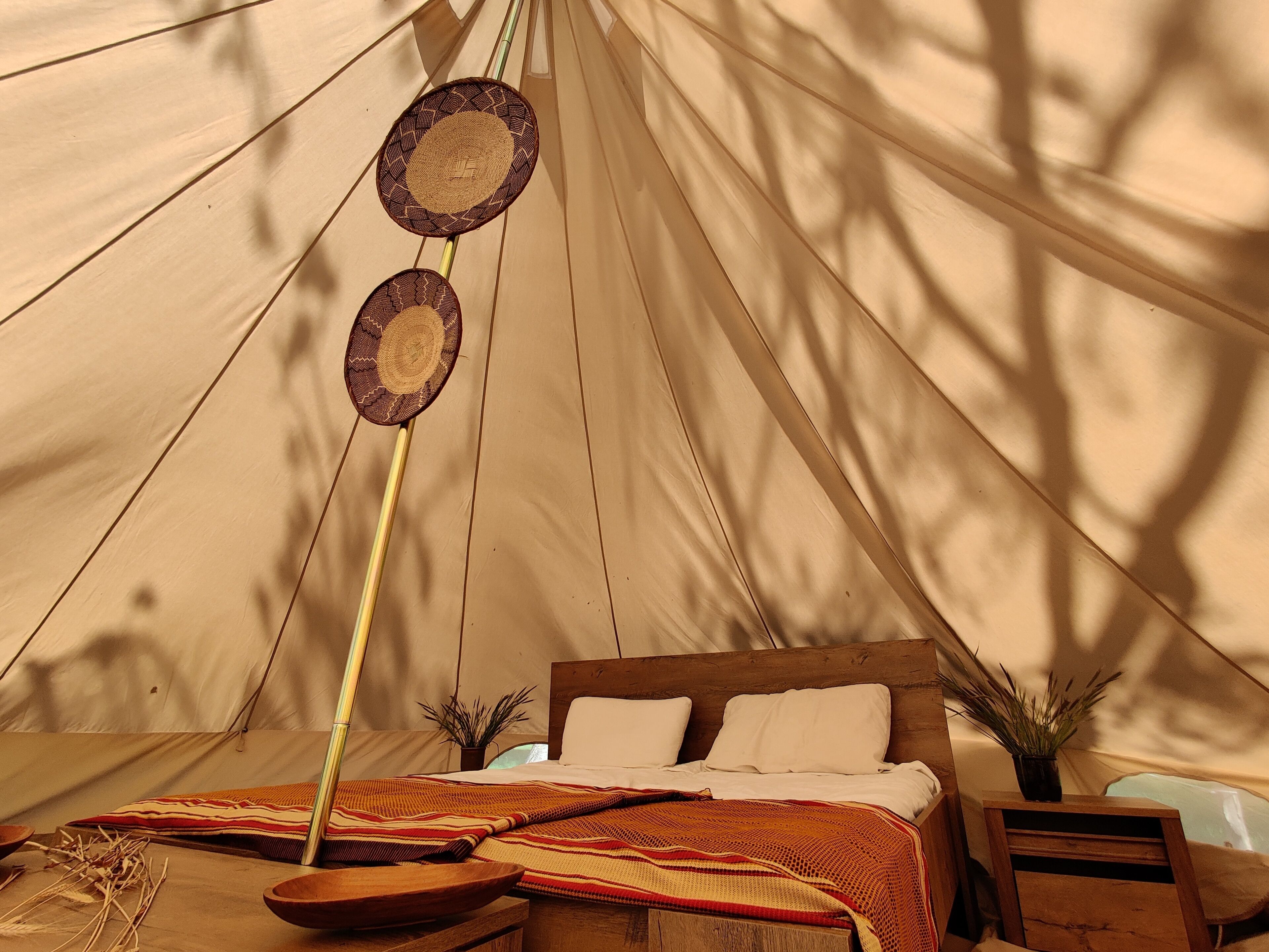 A tented accommodation with a bed, a hanging lamp, and a woven basket.