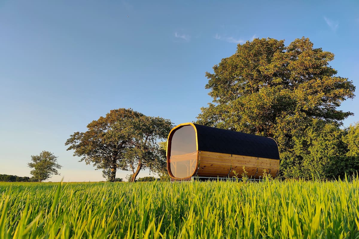 Una estructura cilíndrica en un campo con árboles al fondo.