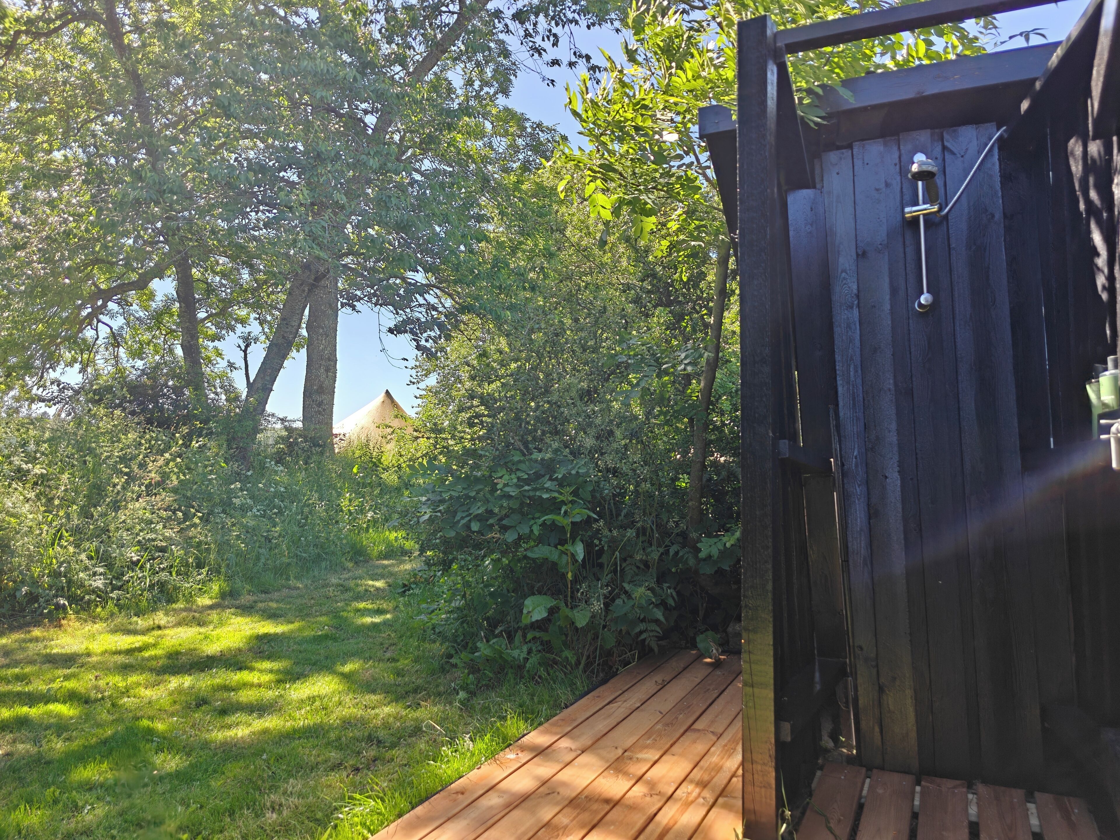 A wooden deck leading to a dark wooden gate, surrounded by lush greenery and trees.