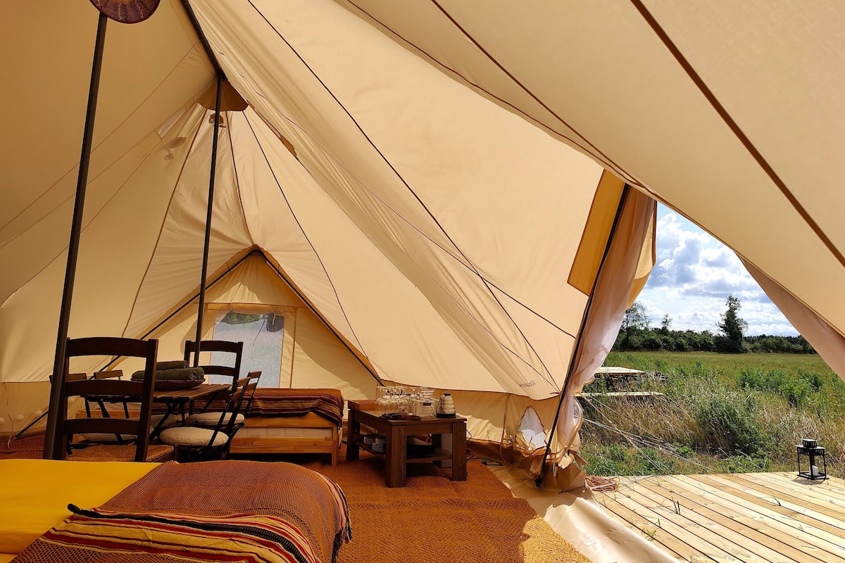 Una carpa con una cama, sillas, una mesa con vasos y vistas al exterior.