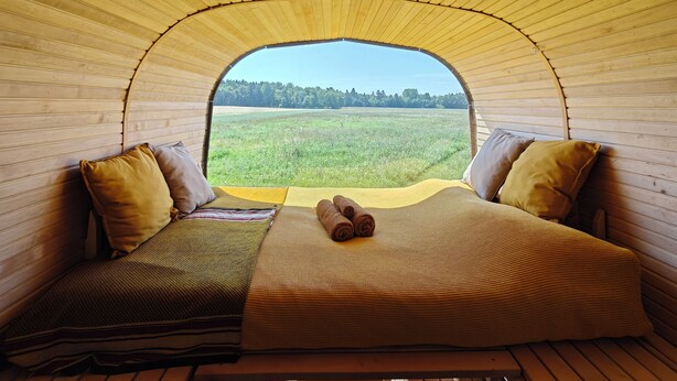 A cozy interior with a bed, pillows, and a view of a green field through a semi-circular opening. - Under Canvas Bornholm (Østermarie)